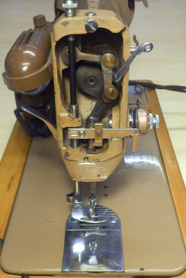 The arm end mechanism of a classic Singer 185K. The tensioner and thread take-up lever are on the right, while the lamp and presser foot lever are on the left.
