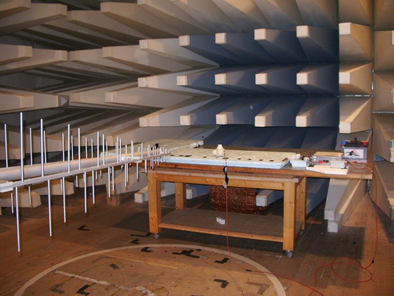 The interior of a typical EMC lab showing the RF-absorbing baffles on the wall, the equipment under test on a wooden table, and a wideband log-periodic antenna. Techie2 [CC-BY-SA-3.0 ], via Wikimedia Commons.