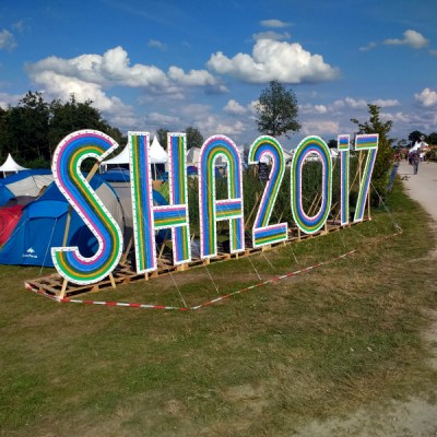 The SHA2017 sign against a blue sky with fluffy clouds.