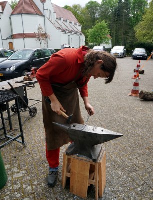 My usual forging attire of steel toecap workboots, spark-resistant overalls, and blacksmith's leather apron. The forge is outside Hack42 hackerspace, Arnhem, and is set up a bit too low for me. Photo: (c) Martina Short, used here with permission.