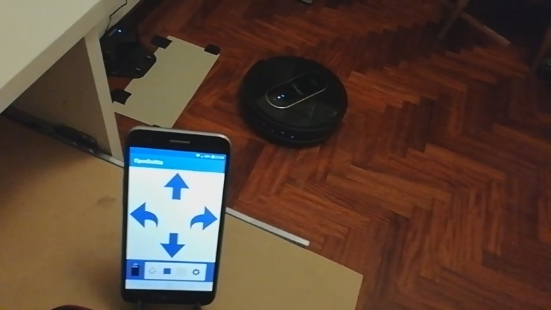 A smartphone with a robot vacuum in the background