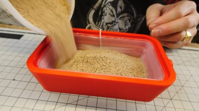 Adding sand to a partially-cured silicone piece so it will take the shape of the expanded mold.