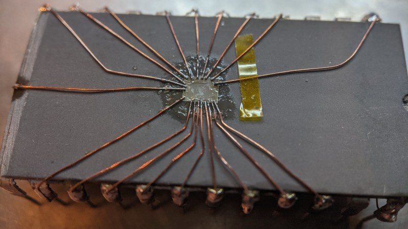 The decapped chip on top of some other DIP IC, with magnet wire soldered to the die, other ends of the magnet wire soldered to pins of the "body donor" DIP IC.