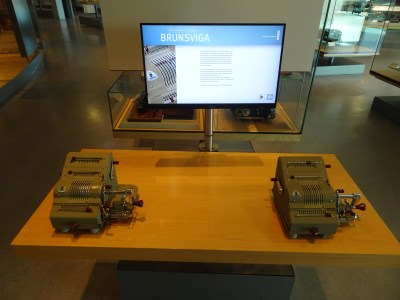 Two mechanical calculators, with a computer monitor displaying instructions behind them