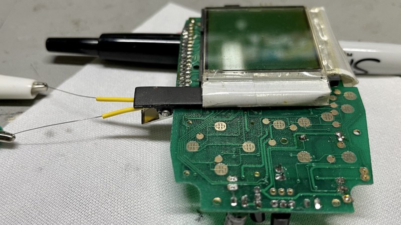 The hairclip-embedded tool being used on a Tiger 99x game console, clipped onto a spot where the plastic ribbon meets the LCD panel itself, heating it up