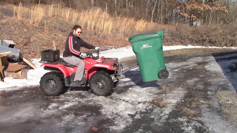 ITman496 in his ATV, using the trashcan lifter to lift a trashcan up in the air. The lifter is a contraption mounted to the front of his ATV, welded together with square tubing