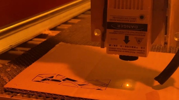 The laser module shown cutting shapes out of a piece of cardboard that's lying on the CNC's work surface