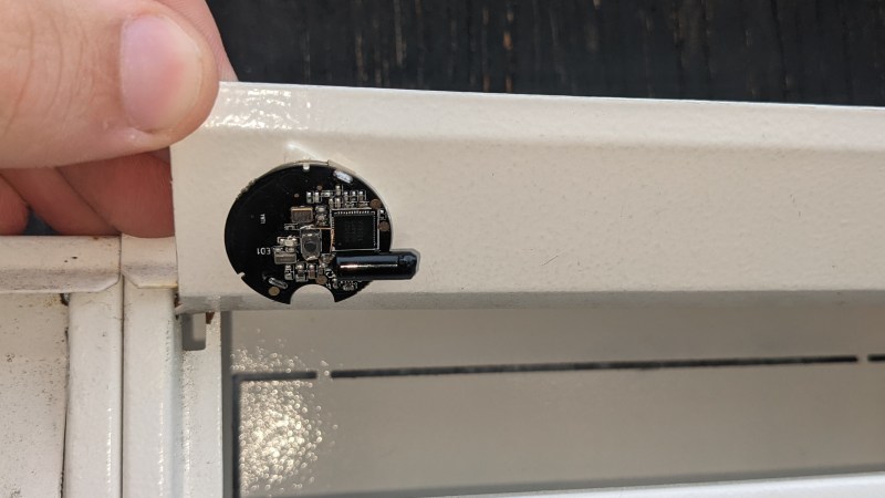 A small round NRF51822 board glued to the underside of a mailbox lid, with a small vibration sensor attached
