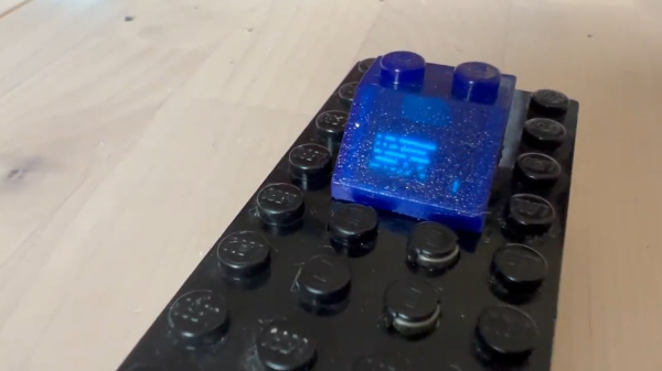 The blue LEGO brick described, with the OLED inside shining through the 3D-printed and subsequently cast brick body. The picture on the small OLED imitates the lines of text shown on the brick that this is an imitation of.