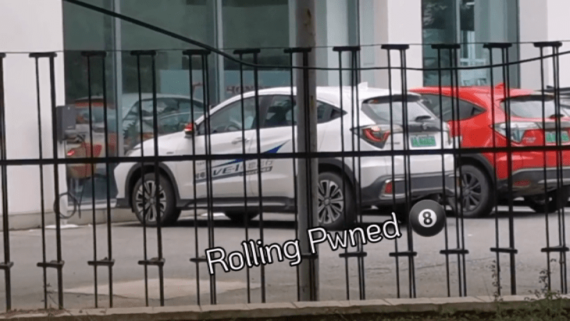 A Honda car behind a gate, with its turn signals shown blinking as it's being unlocked by a portable device implementing the hack in question. Text under the car says "Rolling Pwned".