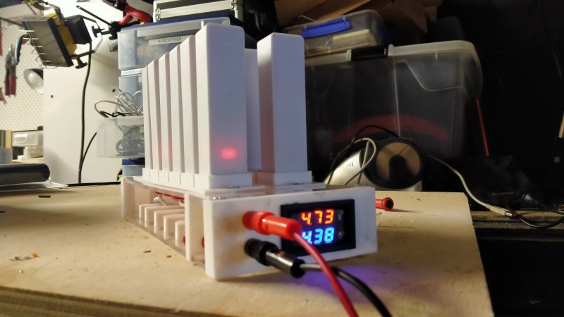 The charging station on the table, with twelve powerbanks plugged into it, charging. A small meter on the front panel shows 4.73 volts and 4.38 amps.