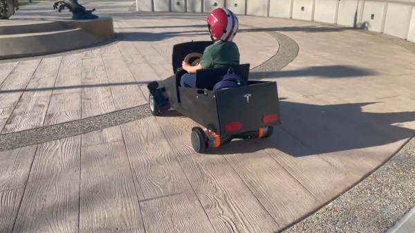 Mahmut's kid in a helmet, riding the go-kart outside on pavement