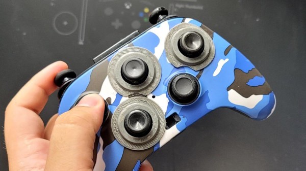 The controller being held in its creator's hand after the modification's been done. The controller is painted in blue-white-black camo-like style. Analog sticks are sticking out where the buttons used to be