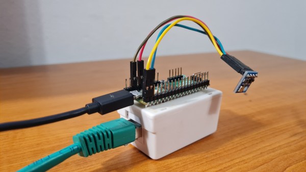 The Pi Pico board on top of a white box with an Ethernet jack, with a sensor module plugged onto the Pico's pin headers. A black MicroUSB and a green Ethernet cable are connected to this device.