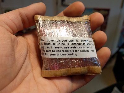 a pack of through-hole resistors wrapping something wrapped in violet bubble wrap, presumably, a LiIon cell. A sticker on top of the whole bundle says "dear buyer, pls you open it, battery is in it, because China is difficult to ship battery, so I have to use resistors to pack it. It is safe to use resistors for packing. thanks for your understanding".
