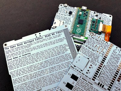 three PCBs being shown - one soldered-together version with a Pico on it, and two upopulated PCBs, showing front and back, on the populated PCB, you can see the Raspberry Pi Pico and other components soldered on. On the unpopulated PCBs, you can see there's a lot of text helping you understand and assemble this e-reader.