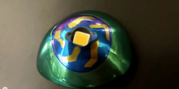 A prosthetic eye anodized green around the edges with a yellow and blue "iris" surrounding an LED center.