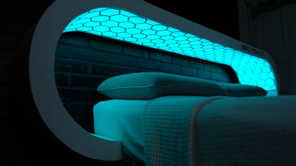 A futuristic bed headboard has a continuous light with a hexagonal grid overlaid on top of it that wraps around the bed, much like an ovoid MRI machine.