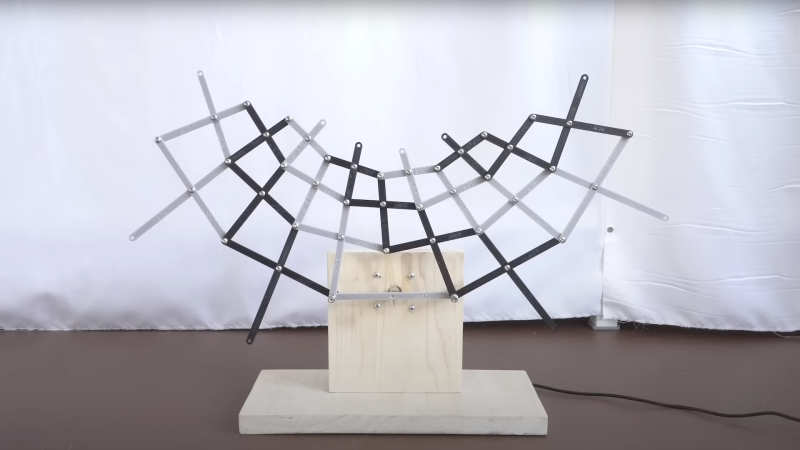 a kinetic bar framework mounted on a wooden base made of 3d printed bars of alternative black and grey color, each joined with m3 bolts and nuts