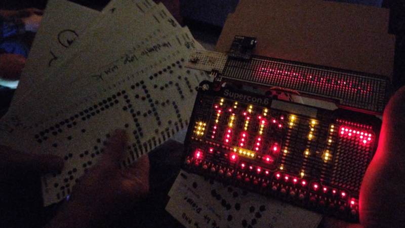 Hackaday supercon badge PCB showing illuminated activity lights after being loaded with a punch card