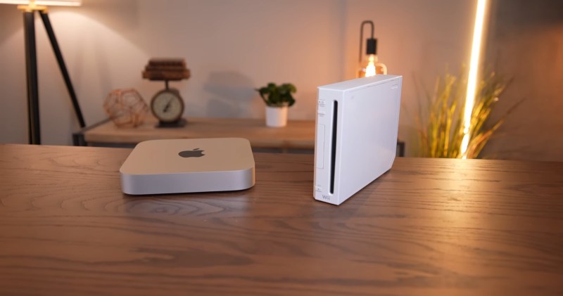 An M1 Mac mini sits next to a white Wii on a wooden table. In the background are various Edison-style LED light fixtures with an incadescent-like light profile.