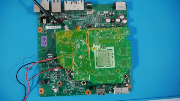 A green highlight emphasizes a cut-down XBox 360 motherboard on top of an intact board. The cut-down board is less than half the size of the intact one.