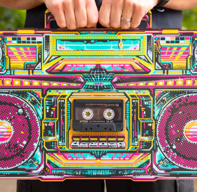 The front of a PCB boombox being held at the top, with a cassette tape in the middle