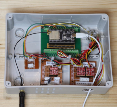 An esp32 module connected to three level shifters inside of a grey utility junction box with a USB power connector coming in powering the ESP32 device and an external wifi antenna mounted on the outside of the junction box, all siting on a wooden table