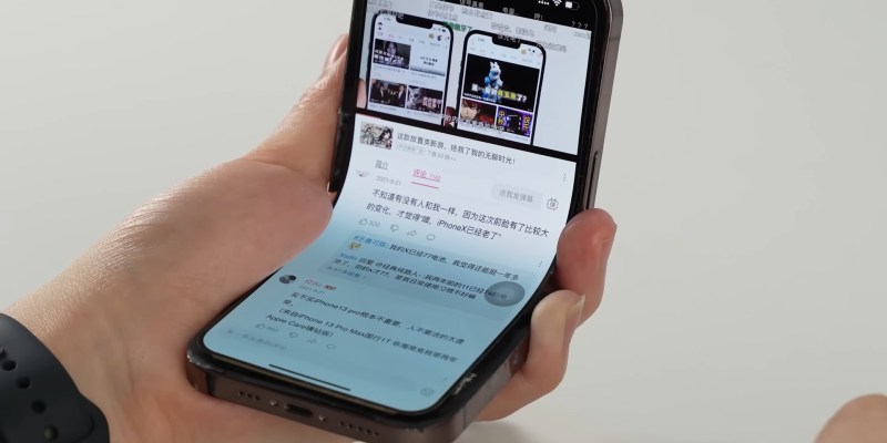 An iPhone sits in a users hand open to the YouTube app. What is unusual is that the iPhone is bent in an L shape and is still functioning properly.