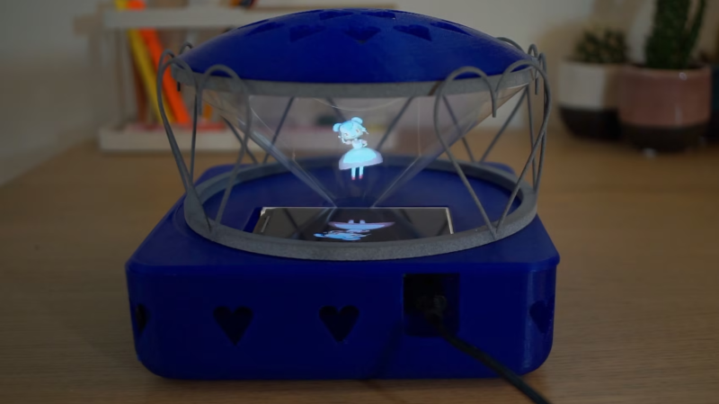 a 3d printed case, sitting on a table with cactuses in the background, with a 3d rendered holo assistant reflected in a cone of polycarbonate sheets from a flat HDMI display pointed up