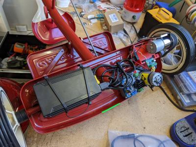 The underside of the back axle of a red radio flyer tricycle with electronics for, two motors and a battery pack 