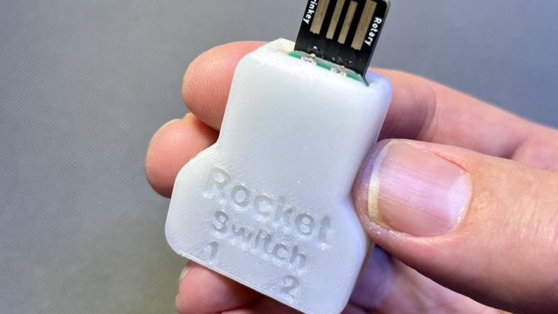The fully assembled RocketSwitch, with a 3D printed case on it and a USB-A connector sticking out, being held in someone's hand.
