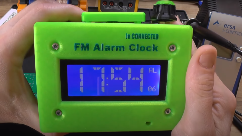 Two hands holding a 3d printed alarm clock with an LCD display, snooze button and knob on top