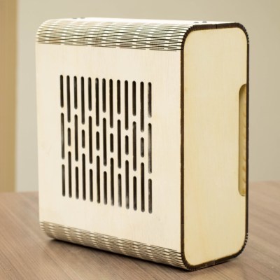 A lasercut wood PC case standing upright on its edge. A series of cuts along the corners allow for the case to be curved instead of purely right angles. One side has substantial cutouts for ventilation.