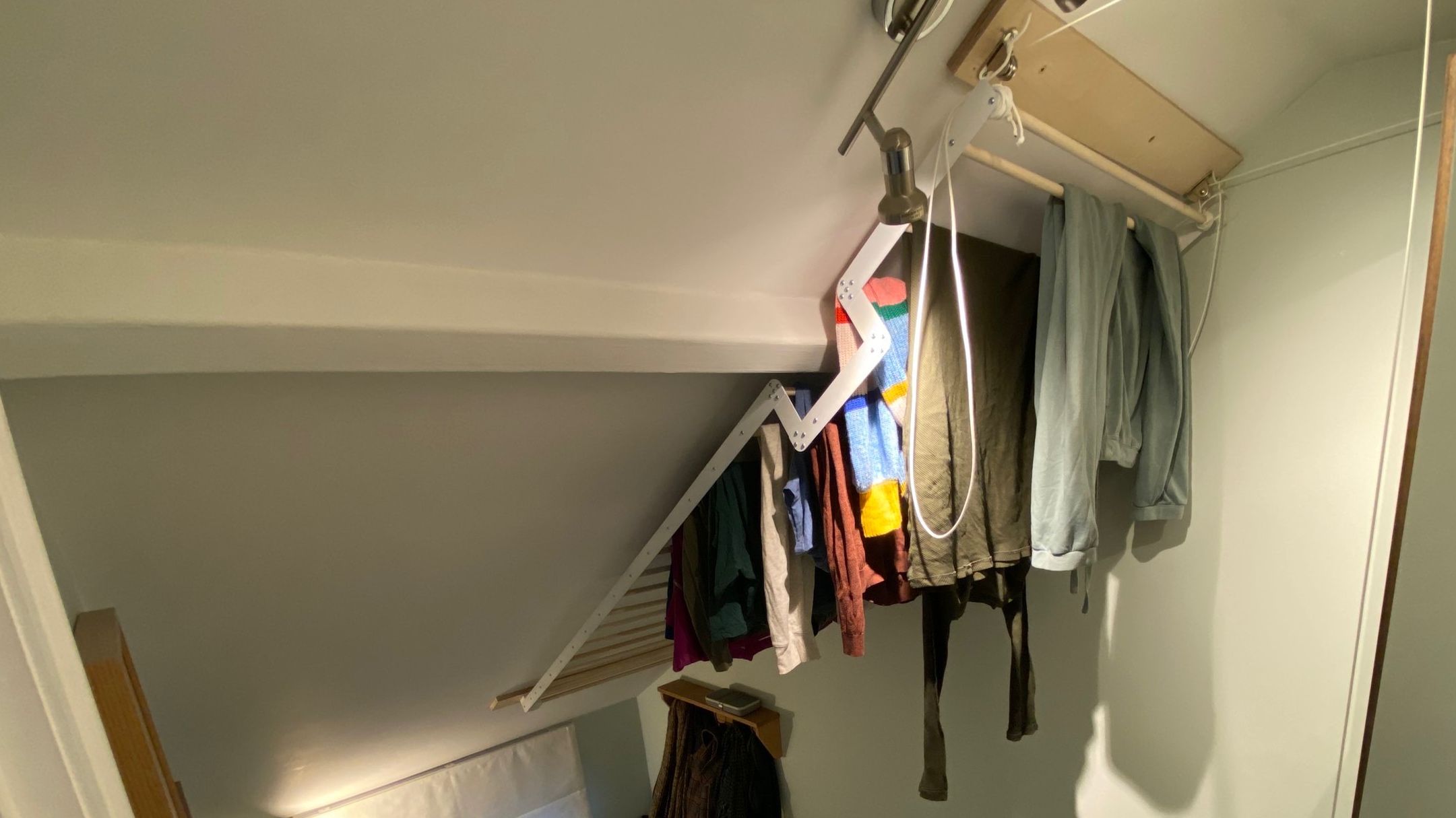 A white stairwell ceiling with a rack holding clothes. The rack follows the slope of the ceiling and is attached to a series of ropes and pulleys to let it got up and down.
