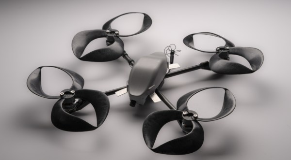 A black quadcopter sits on a grey surface. In place of traditional propellers are four figure eight propellers with sharp tips where the top and bottom of the eight would be.