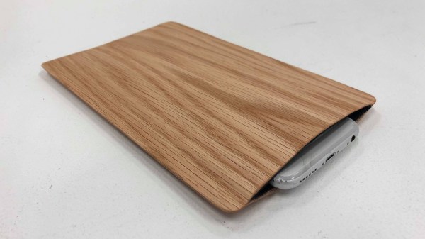 A grey smartphone sits inside a sleeve made of light brown wood veneer and a black felt interior.