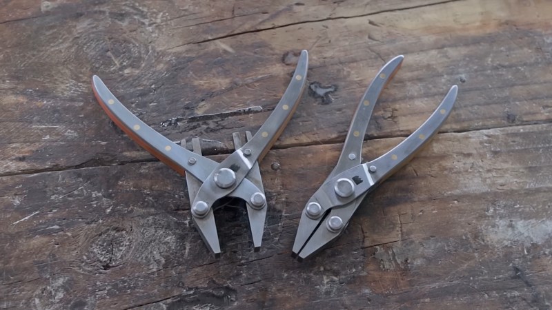 Two pairs of steel parallel pliers sit on a rough wooden benchtop. The pair on the left is open and the pair on the right is closed, demonstrating the parallel nature of the pliers' jaws over their entire range of motion. There are three brass pins flush with the steel surface of the handles and you can just barely make out the brass and copper filler material between the steel outer surfaces of the handles.