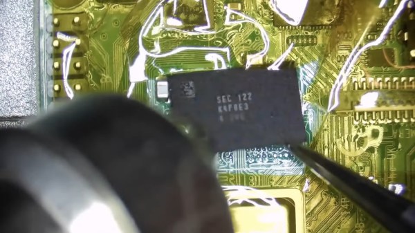 Showing a RAM chip being removed from a Pi 4 board, hot air gun in the shot. Area around the chip is covered with kapton tape.