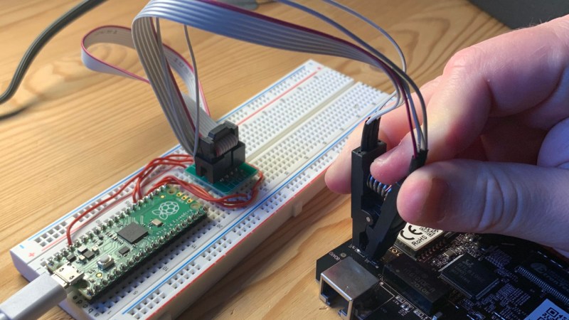 A Pi Pico plugged into a breadboard, with jumpre wires going away from its pins to an SPI flashing clip, that's in turn clipped onto an SPI flash chip on a BeagleBone board
