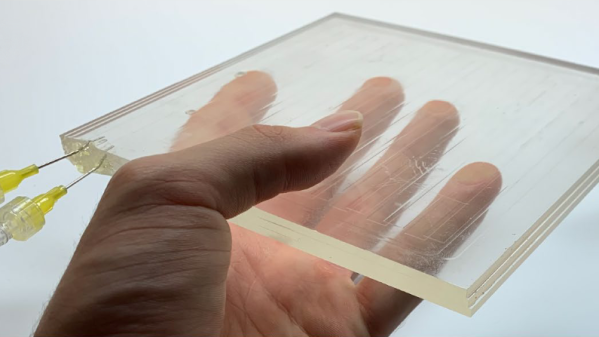 A human hand holds a stack of several plexiglass sheets with needles glued into the ends. Very faint lines can be seen in the transparent stackup.