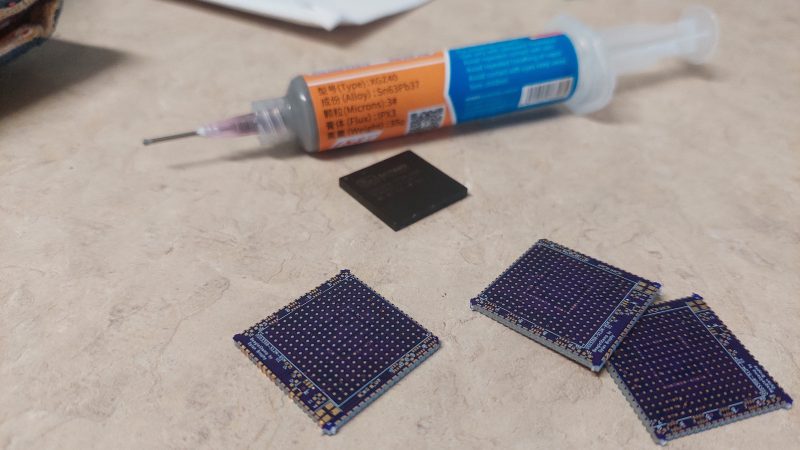 Four square, unpopulated purple PCBs sit in front of a tube of soldering flux on a light grey work surface. The PCBs are only 1"x1".