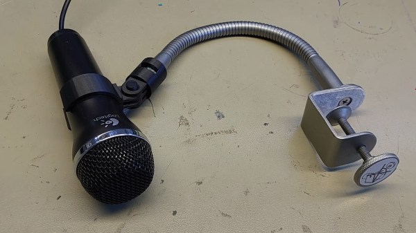 A small black microphone in a black 3d printed mount. The mount is attached to an adjustable silver neck attached to a desk clamp from an IKEA lamp.