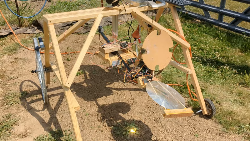 A wooden robot with a large fresnel lens in a sunny garden
