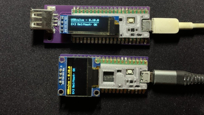 two USBValve devices on a table, both with a USB cable plugged in. The top one with a long narrow OLED display and the bottom one with a 128x64 OLED display.