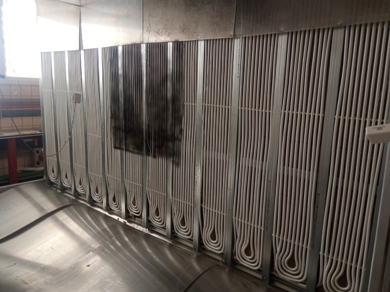 A series of tubes wound up and down as modules in a metal-framed, free-standing wall. The wall is inside a climate-controlled test chamber with a series of differently-colored tubes running behind the free-standing wall.