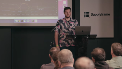 Image of the presenter on the podium, in front of the projector screen with graphs shown on it