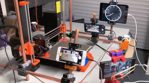 A workbench with a 3D printer, a home-made frame of metal tubing and 3D printed brackets and phone holders. 3 iOS devices and 1 Android phone arranged around the printer with a clock and 3 different camera angles around the print bed