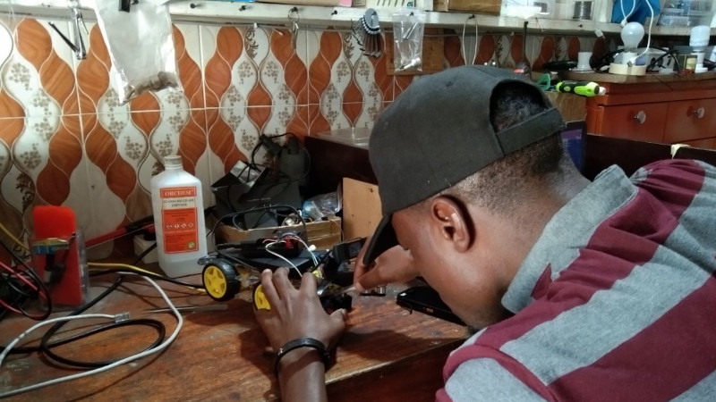 African man hunched over a small robot car chassis