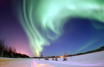 A blue-green aurora against a dark purple and black sunset over a snowy landscape